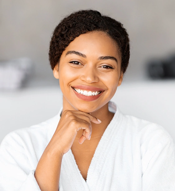 Joyful Black woman in spa robes showcasing radiant skin.